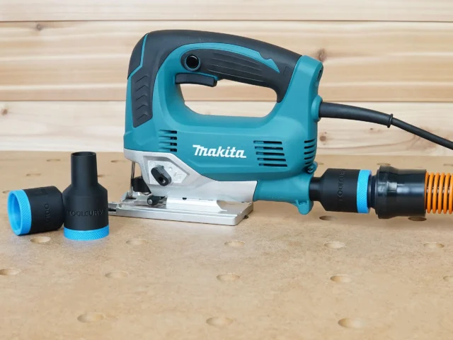 Black ToolCurve 1-1/4" hose adapter with blue ring attached to a Makita jig saw dust port, spare adapter alongside