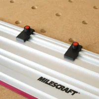 Two black limit stops with red-capped knurled knobs mounted in the slot of a Milescraft guide rail on MDF