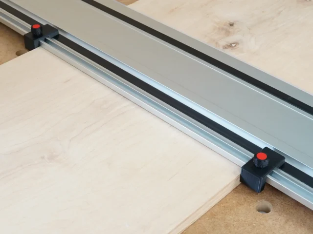 Two black drop stops with red knobs mounted on a Milwaukee track saw guide rail positioned at workpiece edges