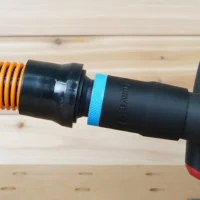 Black 1-1/4 inch hose adapter with blue grip ring joining an orange hose to a Milwaukee track saw port