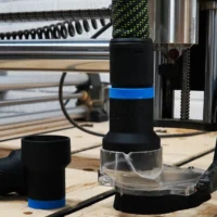 Black hose adapter with blue band installed on Onefinity CNC dust boot, showing adapter opening and two detached sleeves on workbench
