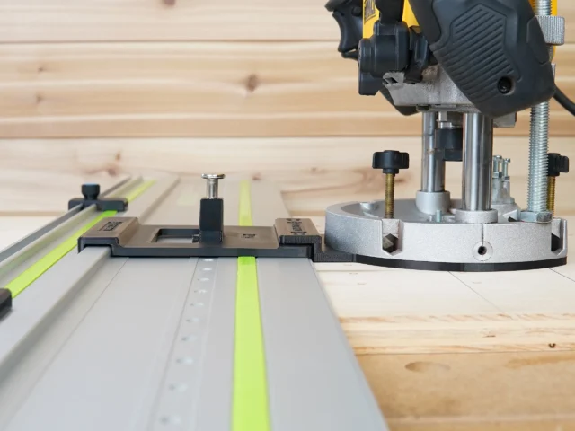 LR 32 hole drilling system mounted on a DeWalt 625 router positioned over a track saw rail, showing the plunge base plate and spring-loaded knob with guide rail stops