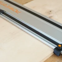 Two black drop stops with orange knobs mounted on a Powertec track saw guide rail, positioned at the ends to align with workpiece edges