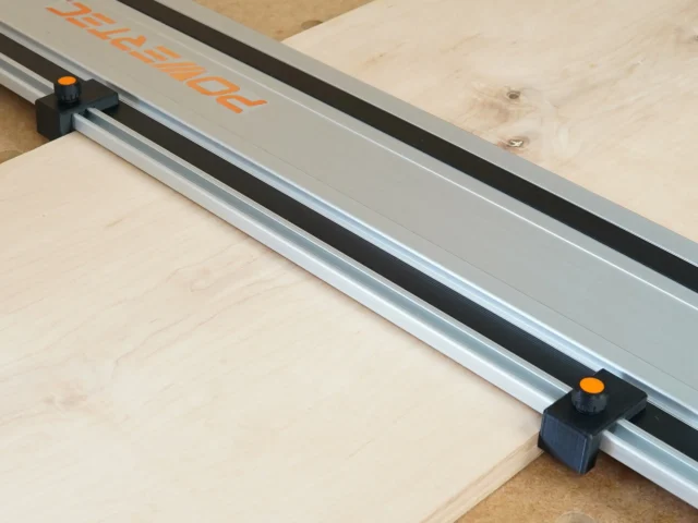 Two black drop stops with orange knobs mounted on a Powertec track saw guide rail, positioned at the ends to align with workpiece edges