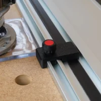 Black limit stop with red knob mounted on a Milwaukee aluminum guide rail, positioned on a cork workbench next to a power tool