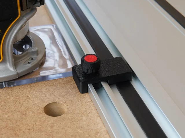 Black limit stop with red knob mounted on a Milwaukee aluminum guide rail, positioned on a cork workbench next to a power tool