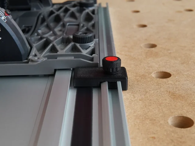 Black limit stop with red knurled knob clipped onto a Milwaukee aluminum guide rail, positioned over a pegboard workbench