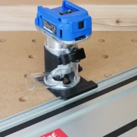 Kobalt 24v router attached to aluminum guide rail on perforated workbench, showing black mounting bracket and clear base detail