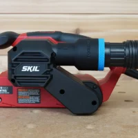 Black ToolCurve 1-7/8 inch hose adapter with blue ring joining a ribbed vacuum hose to a red SKIL belt sander