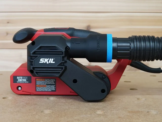 Black ToolCurve 1-7/8 inch hose adapter with blue ring joining a ribbed vacuum hose to a red SKIL belt sander