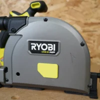Black and yellow dust cover attached to a Ryobi ONE+ HP track saw, with snap-on design visible on the arbor housing