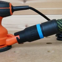 Black hose adapter with blue band attached to orange Black and Decker sander dust port, with braided hose connected behind