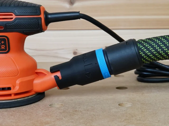 Black hose adapter with blue band attached to orange Black and Decker sander dust port, with braided hose connected behind