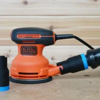 Black ToolCurve 1-1/4 inch hose adapter with blue band, one installed on a Black and Decker sander dust port and a spare standing alongside