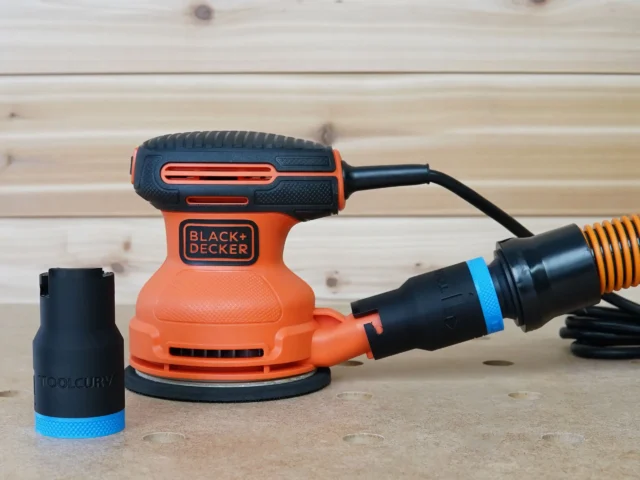Black ToolCurve 1-1/4 inch hose adapter with blue band, one installed on a Black and Decker sander dust port and a spare standing alongside