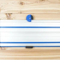 Blue wall mount with white rails and rolling carriage, holding a Kreg ACS track saw rail on wood background