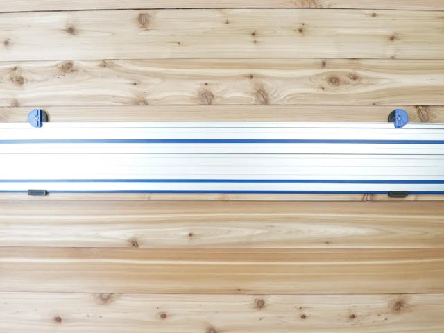 Two blue wall mounts holding a Kreg ACS track saw rail horizontally on wooden wall studs