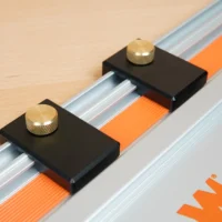 Two black limit stops with brass knurled knobs mounted on a Wen track saw guide rail with orange tape