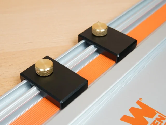Two black limit stops with brass knurled knobs mounted on a Wen track saw guide rail with orange tape