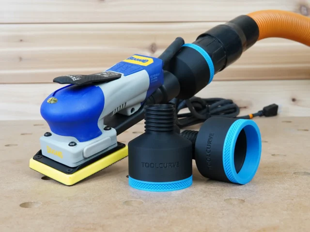 Two black ToolCurve 2-1/2 inch hose adapters with blue ribbed collars beside a blue Ekasand sander and hose