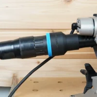 Black ToolCurve 2-1/2 inch hose adapter with blue band joining an orange vac hose to a DeWalt miter saw dust port