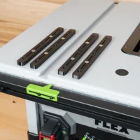 Four brown adjustable miter bars with countersink holes mounted on a Flex table saw, with a lime-green clamp positioned on the front rail