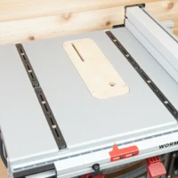 Four adjustable miter bars mounted on a table saw with cream-colored accessory plate between two dark bars, installed on Worm Drive saw