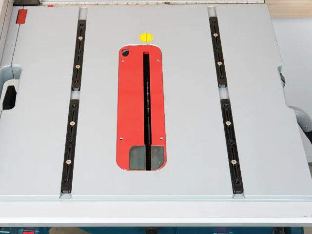 Red plastic miter bar with yellow knob and black slot, positioned centrally on a table saw surface with black adjustment bars on either side