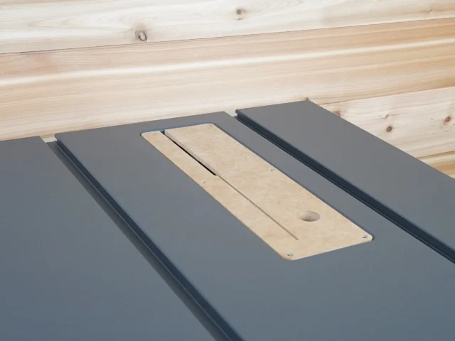 Light wood zero clearance insert with center slot and mounting hole, positioned on dark gray table saw inserts