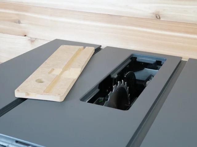 Zero clearance insert for SawStop Compact table saw shown installed in the saw's blade opening, with wooden test piece positioned beside it on the gray table top