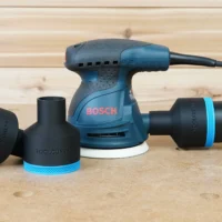 Black ToolCurve 2-1/2" hose adapters with blue trim beside a Bosch 5in sander, one joined to a vac hose