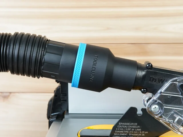 Black 2-1/2 inch ToolCurve hose adapter with blue ring joining a vacuum hose to a DeWalt table saw blade guard port