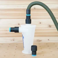 White plastic hose adapter with black threaded ports connected to green mesh hose and Oneida Dust Deputy, shown from front angle on wooden workbench