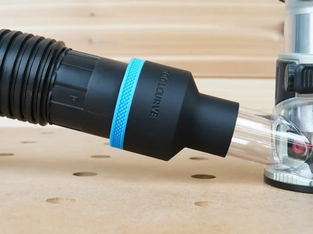 Black ToolCurve 2-1/2 inch hose adapter with blue ring joining a vacuum hose to a Makita trim router dust port