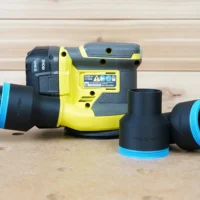 Black 2-1/2 inch ToolCurve hose adapter connecting a vacuum hose to a Ryobi 18v sander, with two spare adapters beside it