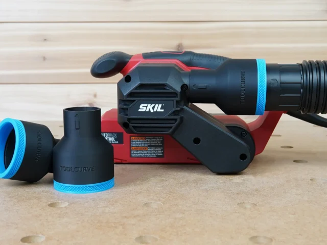 Black ToolCurve 2-1/2 inch hose adapter with blue trim, shown loose beside a SKIL belt sander with another adapter fitted to its dust port