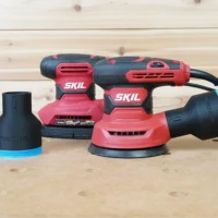 Black ToolCurve 2-1/2 inch hose adapter with blue trim installed on a SKIL random orbital sander, plus a spare adapter alongside