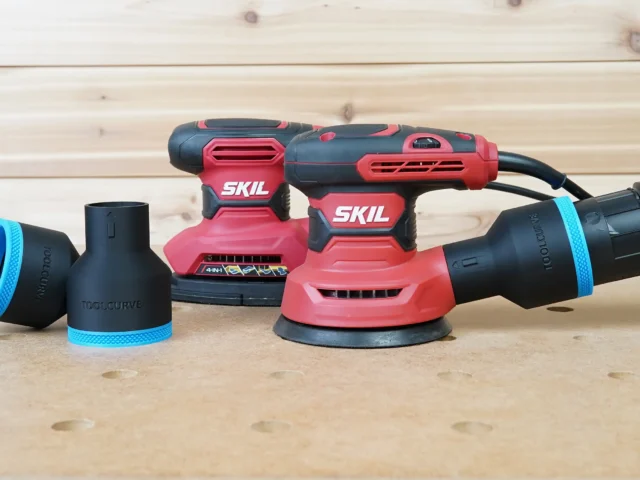 Black ToolCurve 2-1/2 inch hose adapter with blue trim installed on a SKIL random orbital sander, plus a spare adapter alongside