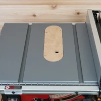 Zero clearance insert installed on Milwaukee M18 table saw, showing rounded MDF insert plate with center opening and mounting screws