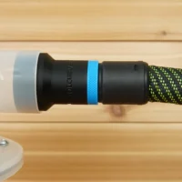 Black plastic hose adapter with blue band attached to green and black braided hose, installed on Cen-Tec dust separator with white cap on wooden bench