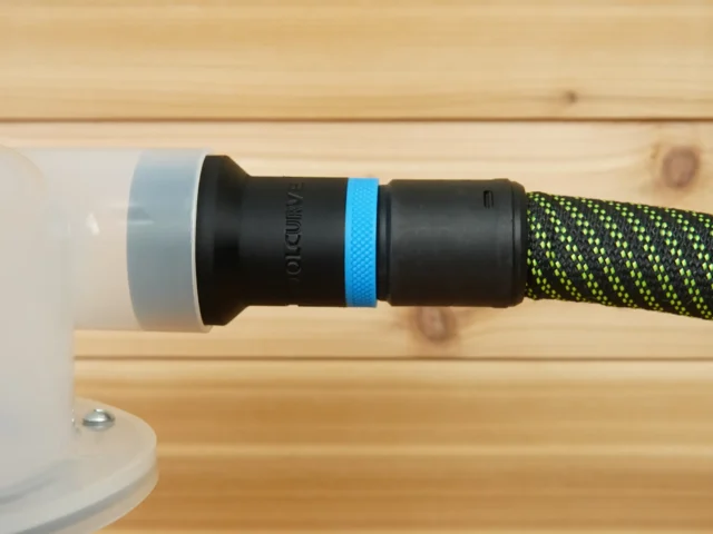Black plastic hose adapter with blue band attached to green and black braided hose, installed on Cen-Tec dust separator with white cap on wooden bench
