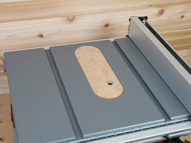 Uncut MDF Dado zero clearance insert seated in a Milwaukee M18 table saw top, screw holes and finger hole visible