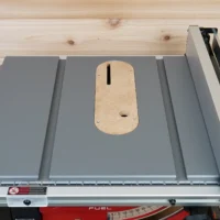 Zero clearance insert with natural MDF face installed on Milwaukee M18 table saw, showing centered slot and mounting hole