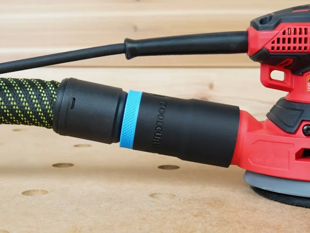 Black hose adapter with blue band attached to Craftsman orbital sander dust port, connected to green and black braided hose