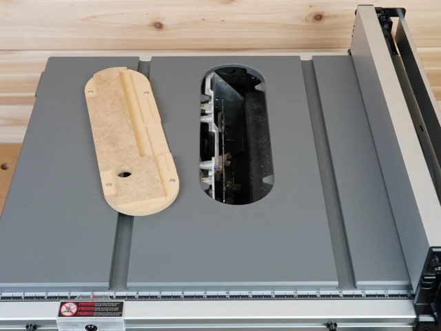 Zero clearance insert for Milwaukee M18 table saw installed in saw top, with wooden insert visible on left and open cutout showing blade area on right