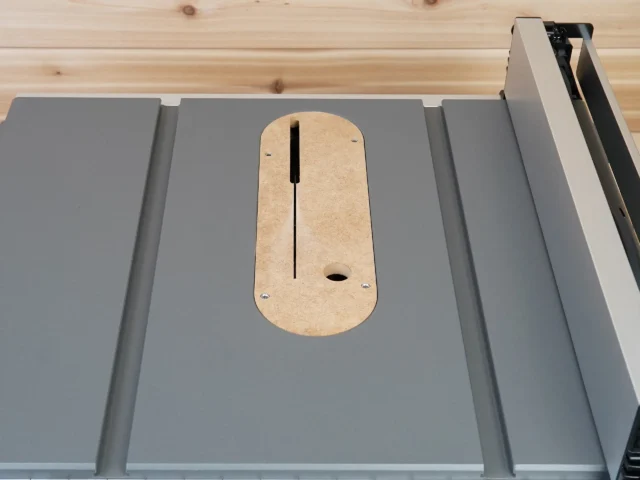 Zero clearance insert for Milwaukee M18 table saw installed on saw table, showing rounded wood shape with vertical slot and offset hole for blade height adjustment