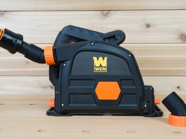 Black plastic no snag dust port adapter attached to Wen track saw, with orange hose connector angled upward and separate hose end port shown alongside