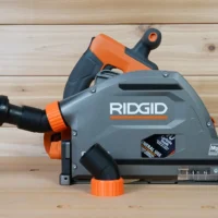 Black and orange no snag dust port adapter mounted on a Ridgid track saw, with orange-banded black vacuum hose attached to the upward-angled port