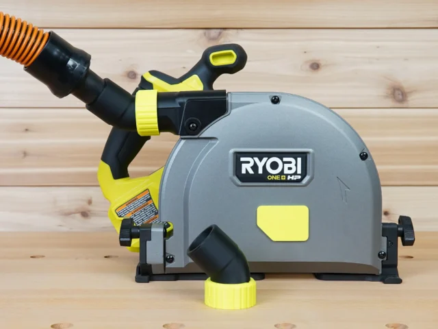No Snag Dust Port for Ryobi track saw attached to a gray and yellow Ryobi saw, with orange hose routed upward away from the track