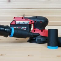 Black ToolCurve 1-1/4 inch hose adapter with blue cuff joining an orange hose to a Milwaukee M18 sander, two spare adapters beside it
